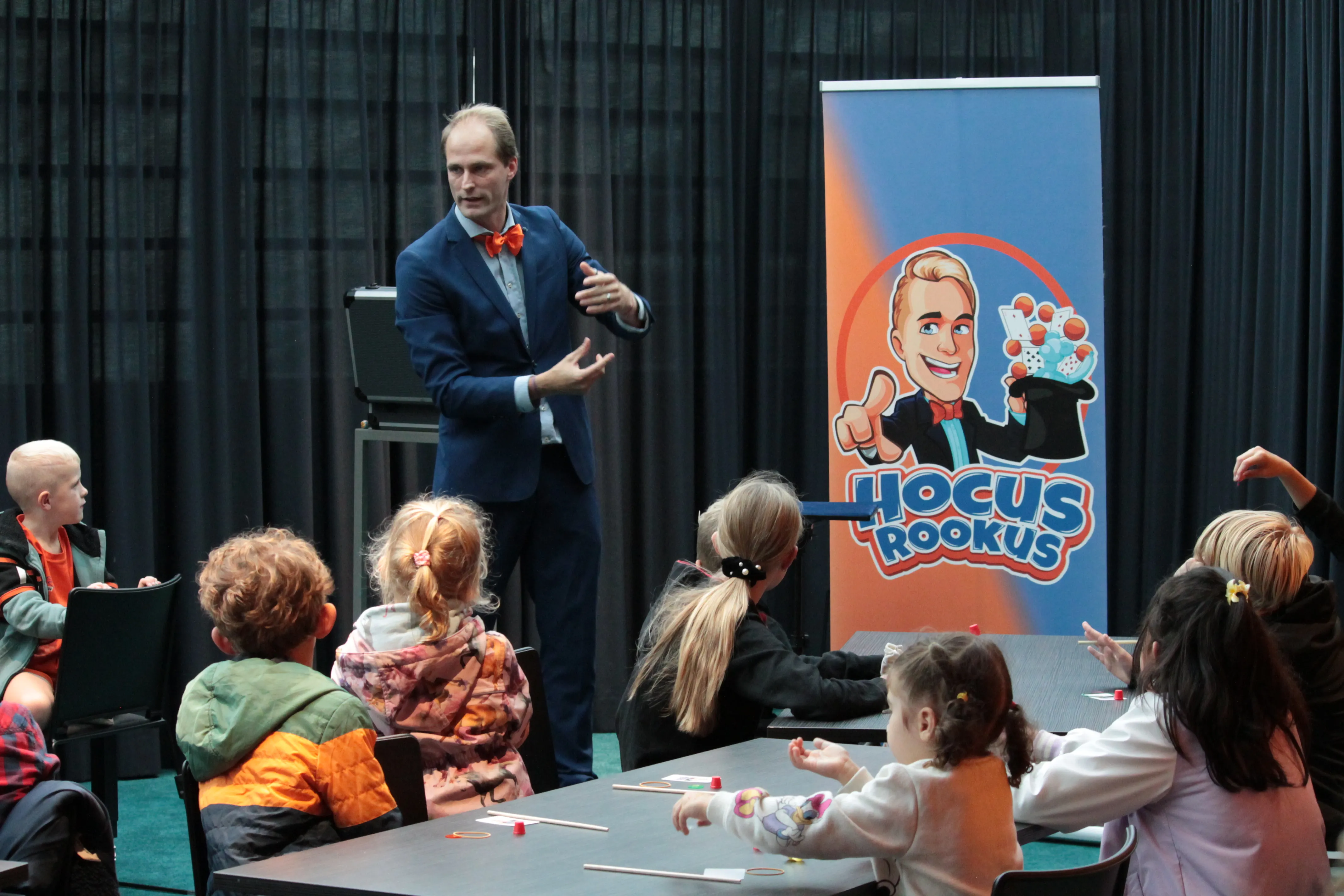 Hocus Rookus goochelt in BSO-zaal voor groep kinderen aan tafel