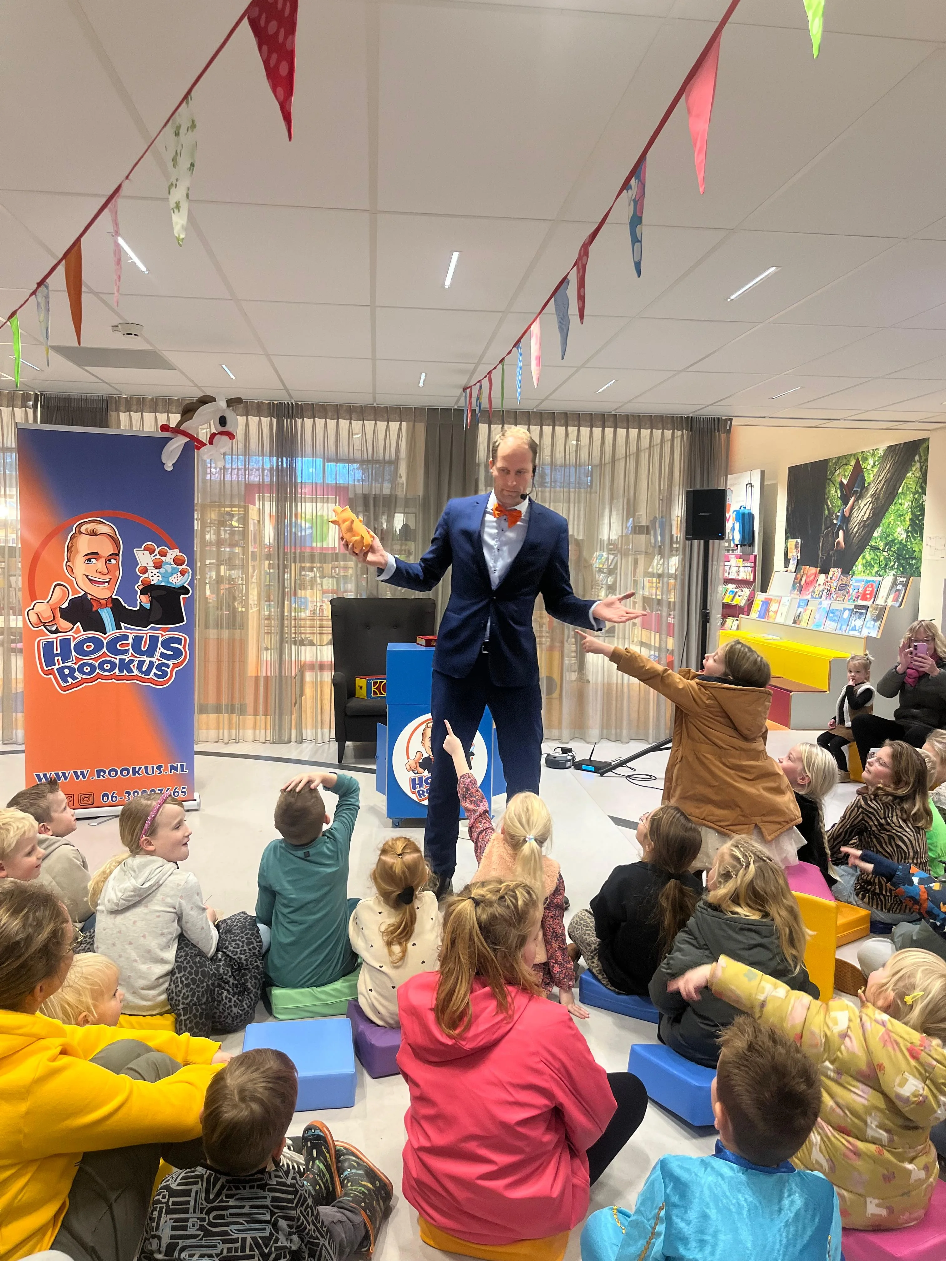 Hocus Rookus goochelt voor groep kinderen bij bibliotheek — kinderen reageren enthousiast