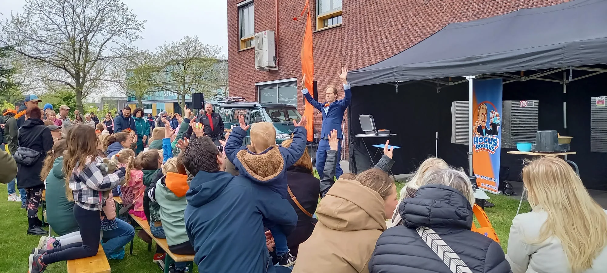 Kindergoochelaar Hocus Rookus leidt groot publiek tijdens buitenshow — armen omhoog
